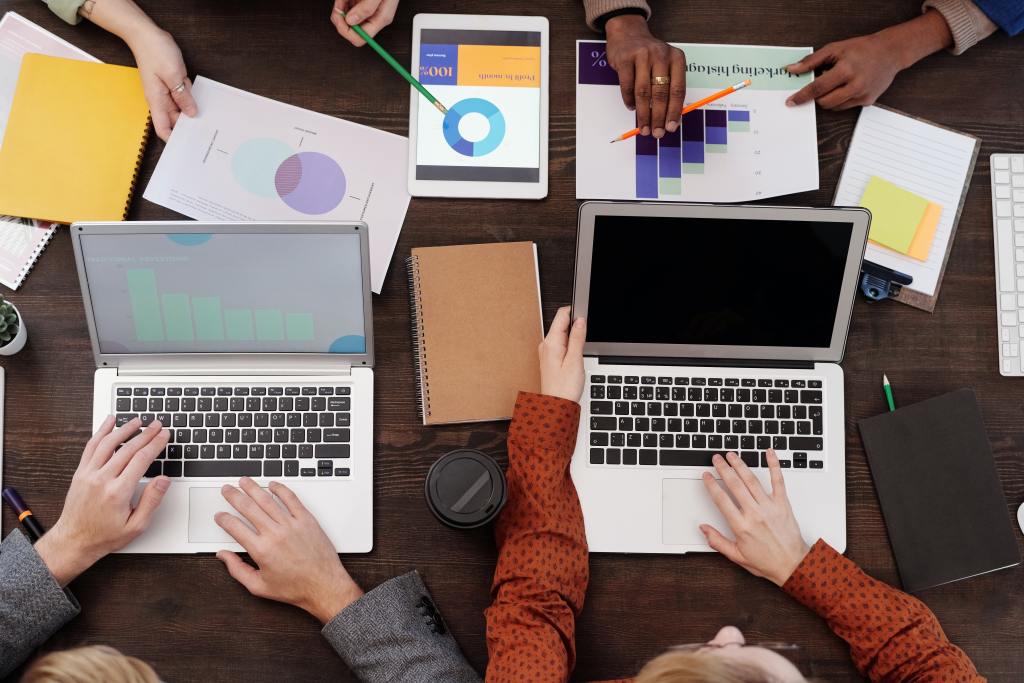 Group of people with laptops or tablets sitting around a table discussing marketing strategy 